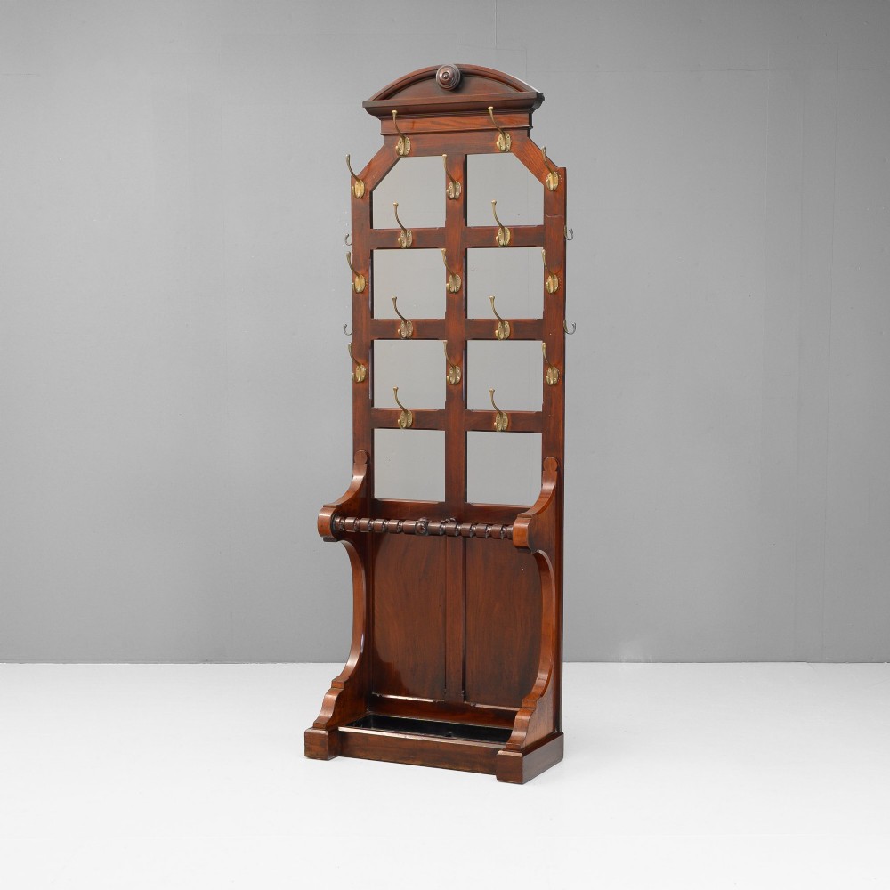 A tall Victorian mahogany hallstand featuring an architectural pediment cresting, multiple brass coat hooks, and a lower stick stand with an integrated drip tray.
