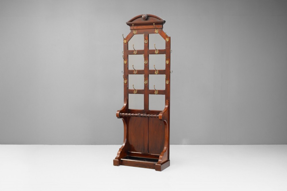 A tall Victorian mahogany hallstand featuring an architectural pediment cresting, multiple brass coat hooks, and a lower stick stand with an integrated drip tray. View II