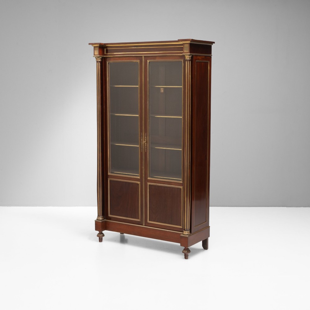 A dark mahogany two-door glazed bookcase featuring brass line inlay, fluted brass-capped columns, and glass doors over solid wood panels.