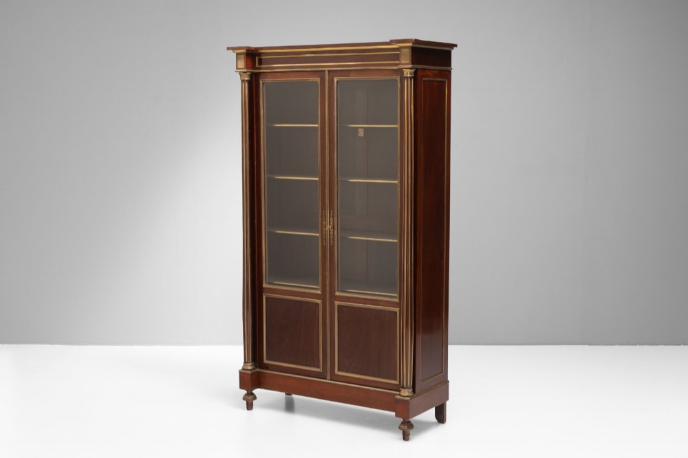 A dark mahogany two-door glazed bookcase featuring brass line inlay, fluted brass-capped columns, and glass doors over solid wood panels. View II