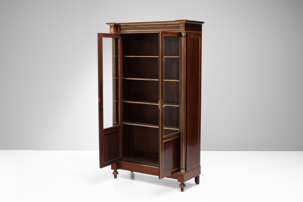 A dark mahogany two-door glazed bookcase featuring brass line inlay, fluted brass-capped columns, and glass doors over solid wood panels. View III