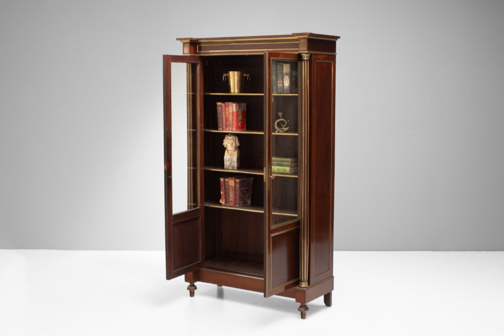 A dark mahogany two-door glazed bookcase featuring brass line inlay, fluted brass-capped columns, and glass doors over solid wood panels. View IV