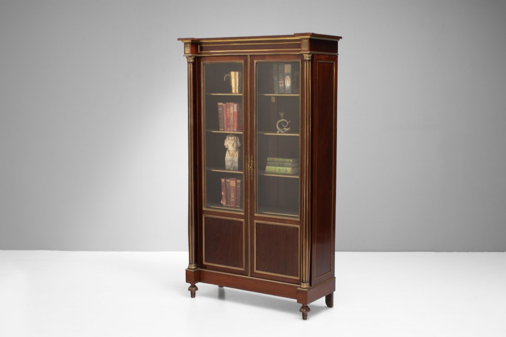 A dark mahogany two-door glazed bookcase featuring brass line inlay, fluted brass-capped columns, and glass doors over solid wood panels. View V