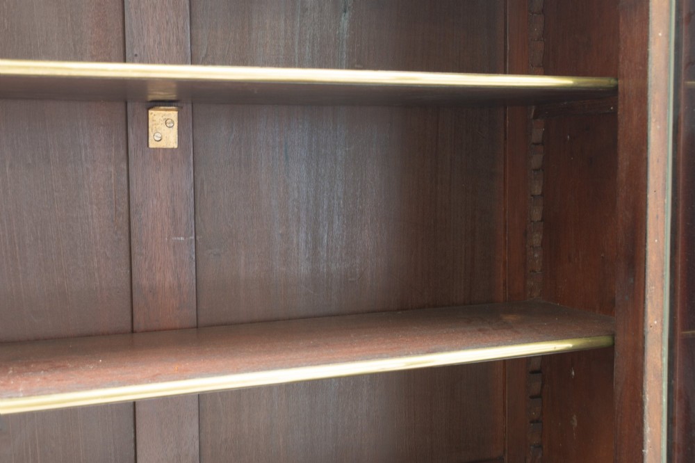 A dark mahogany two-door glazed bookcase featuring brass line inlay, fluted brass-capped columns, and glass doors over solid wood panels. View VI