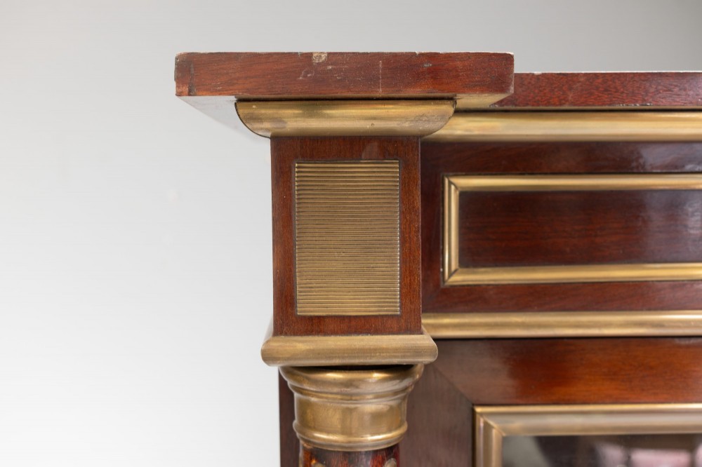 A dark mahogany two-door glazed bookcase featuring brass line inlay, fluted brass-capped columns, and glass doors over solid wood panels. View VII