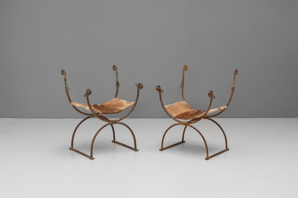 A pair of wrought iron X-frame curule side chairs featuring scrolled metal finials and stretched tan hide sling seats. View II