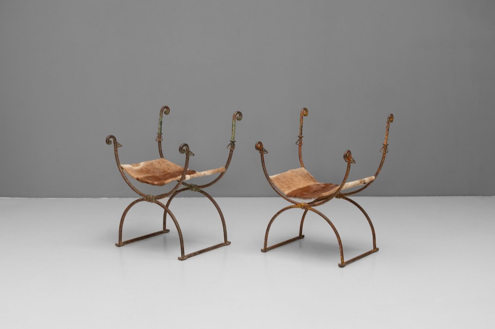 A pair of wrought iron X-frame curule side chairs featuring scrolled metal finials and stretched tan hide sling seats. View III