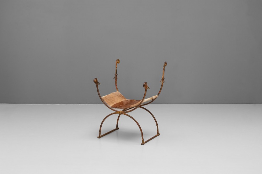 A pair of wrought iron X-frame curule side chairs featuring scrolled metal finials and stretched tan hide sling seats. View IV
