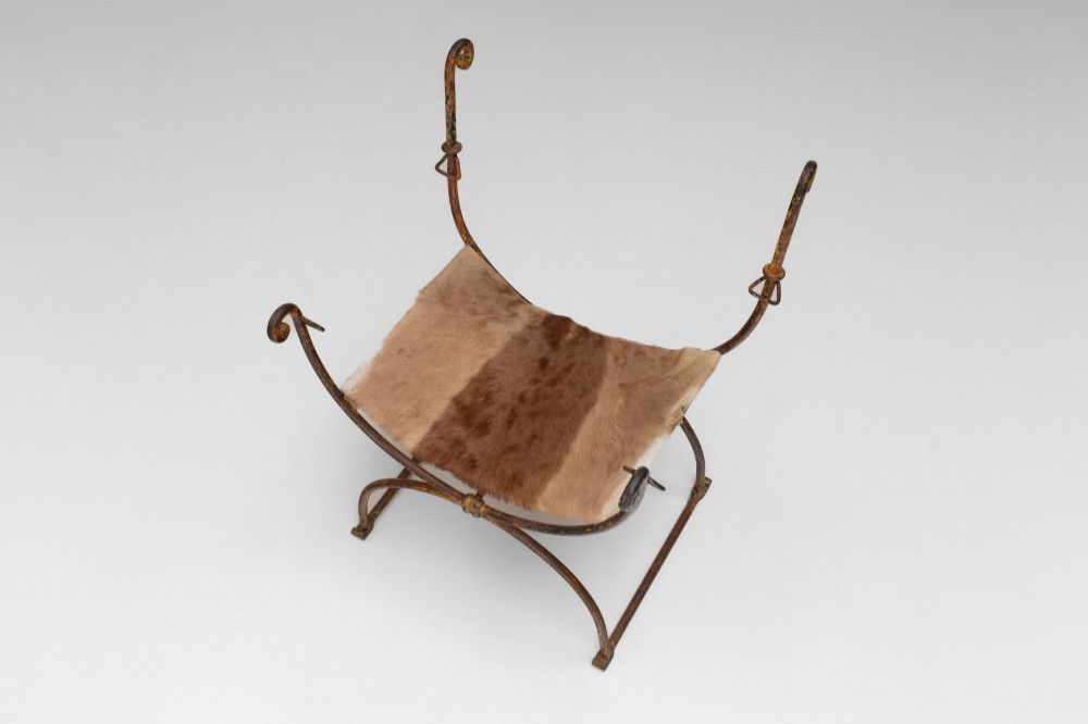 A pair of wrought iron X-frame curule side chairs featuring scrolled metal finials and stretched tan hide sling seats. View V