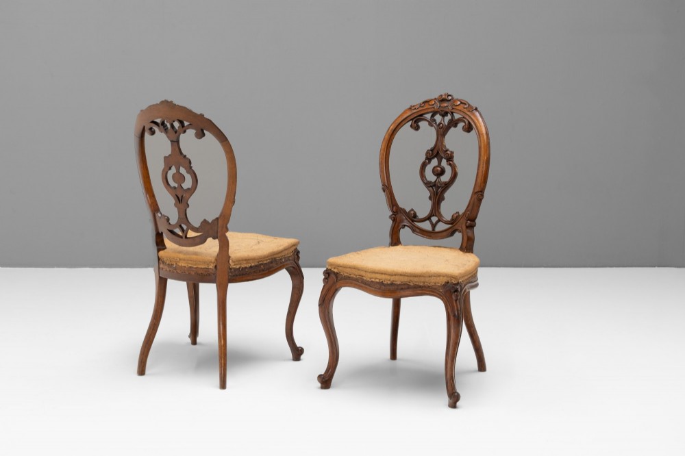 A pair of antique Victorian Rococo Revival carved timber side chairs with balloon backs, open scrollwork splats, cabriole legs, and neutral upholstery. View II