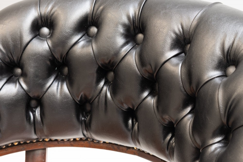 An antique Victorian swivel desk chair featuring a deep-buttoned dark leather backrest, shaped wooden seat, turned arm supports, and splayed legs on brass castors. View V