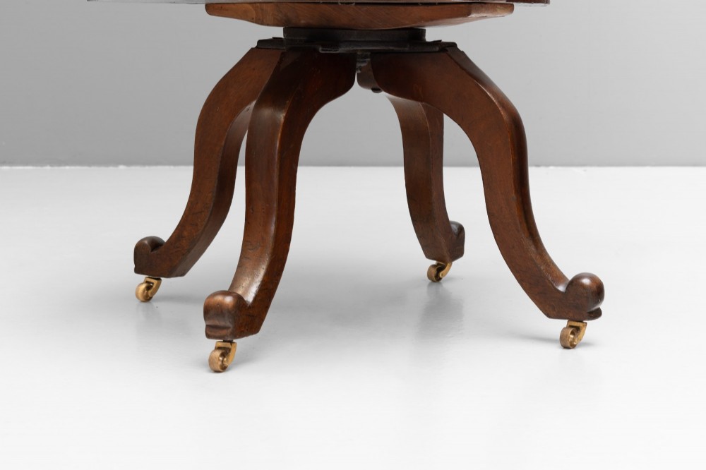 An antique Victorian swivel desk chair featuring a deep-buttoned dark leather backrest, shaped wooden seat, turned arm supports, and splayed legs on brass castors. View IX