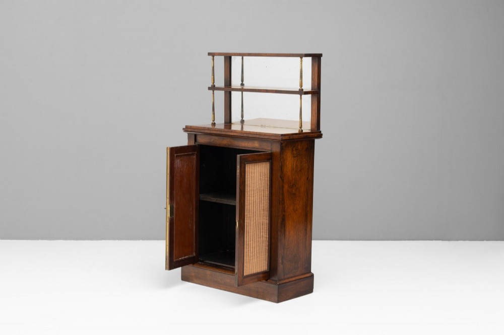 An antique rosewood chiffonier featuring a two-tier mirrored shelf superstructure supported by brass columns over a double-door cupboard with fabric panels. View II