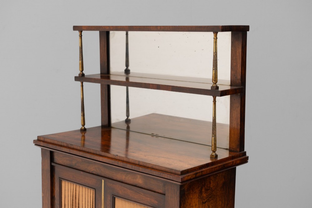 An antique rosewood chiffonier featuring a two-tier mirrored shelf superstructure supported by brass columns over a double-door cupboard with fabric panels. View IV