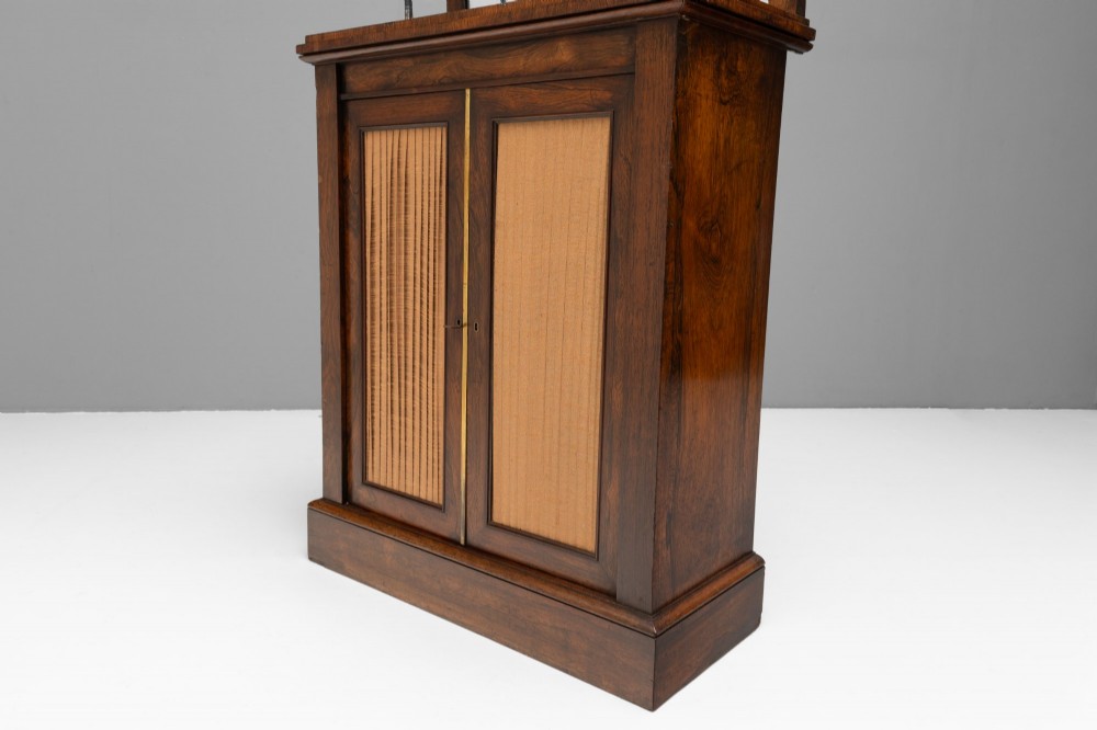 An antique rosewood chiffonier featuring a two-tier mirrored shelf superstructure supported by brass columns over a double-door cupboard with fabric panels. View VI
