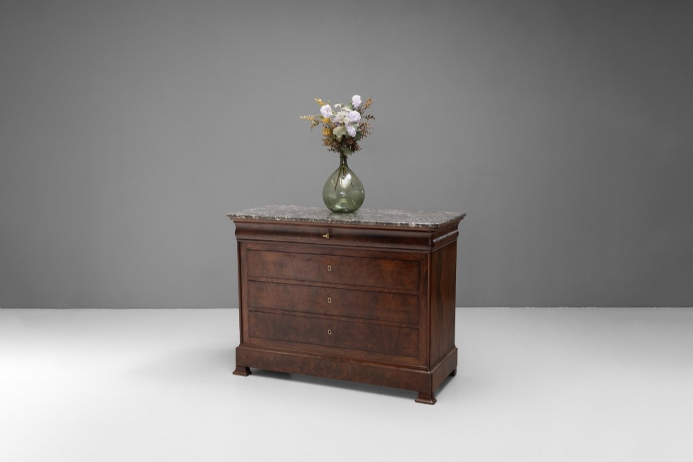 A nineteenth-century French mahogany commode featuring three main drawers, a grey marble top, and brass keyhole escutcheons.