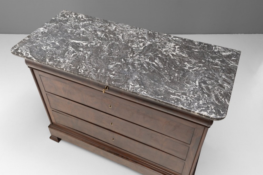 A nineteenth-century French mahogany commode featuring three main drawers, a grey marble top, and brass keyhole escutcheons. View III