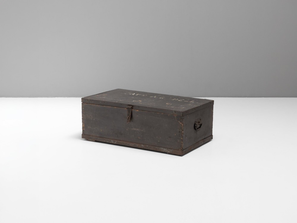 A dark brown rectangular wooden sea chest featuring white painted lettering on the flat lid and iron drop side handles.