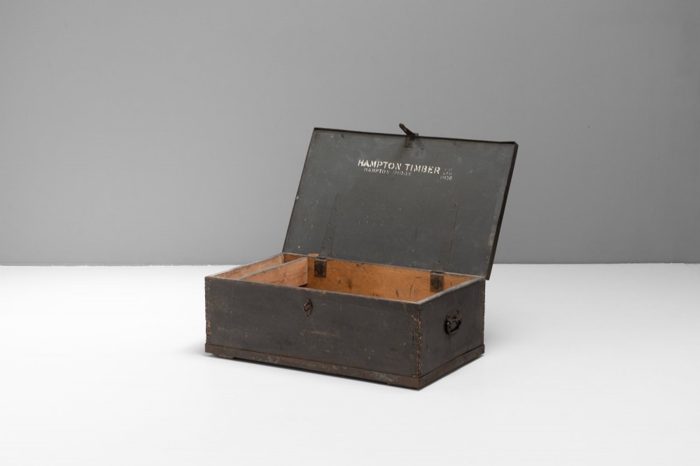 A dark brown rectangular wooden sea chest featuring white painted lettering on the flat lid and iron drop side handles. View II