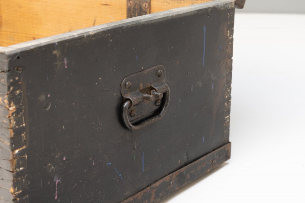 A dark brown rectangular wooden sea chest featuring white painted lettering on the flat lid and iron drop side handles. View VII