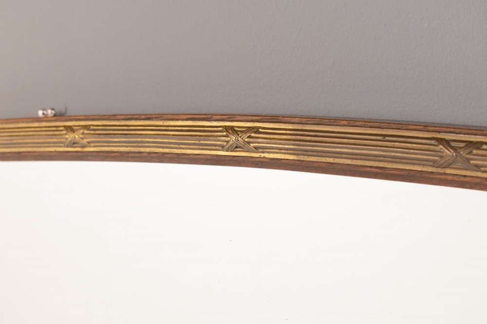 A wide arched overmantel mirror featuring a reeded gilt frame with detailed cross-ribbon motifs and a flat wooden base. View IV