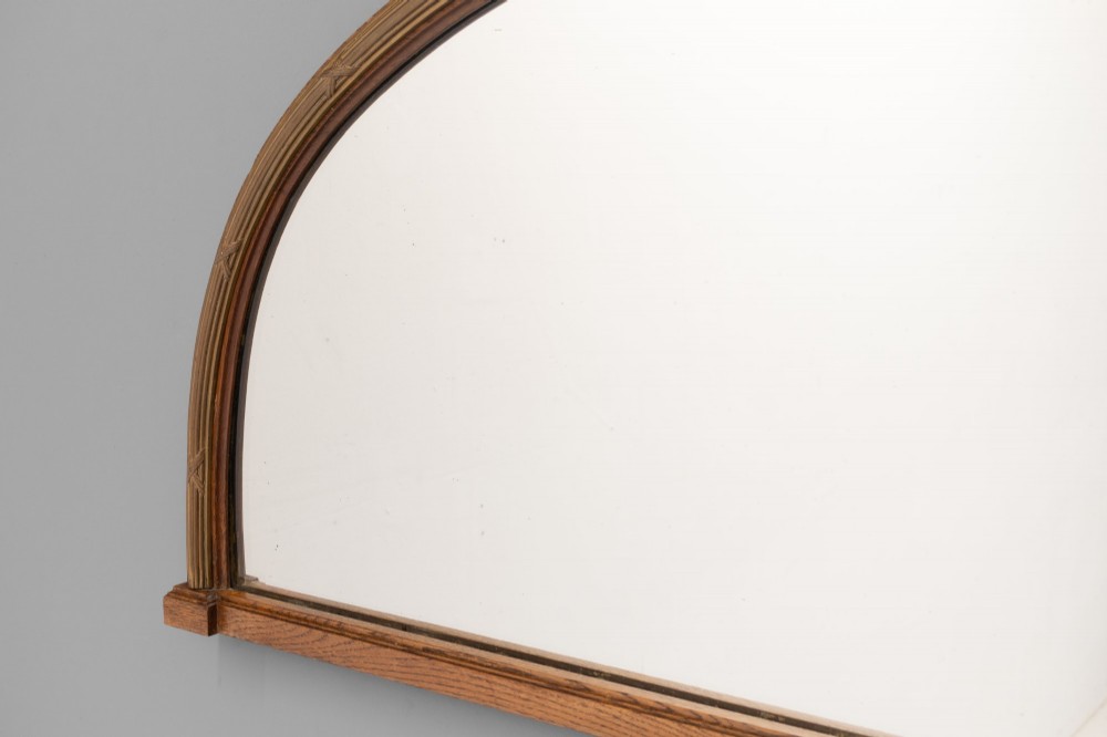 A wide arched overmantel mirror featuring a reeded gilt frame with detailed cross-ribbon motifs and a flat wooden base. View V