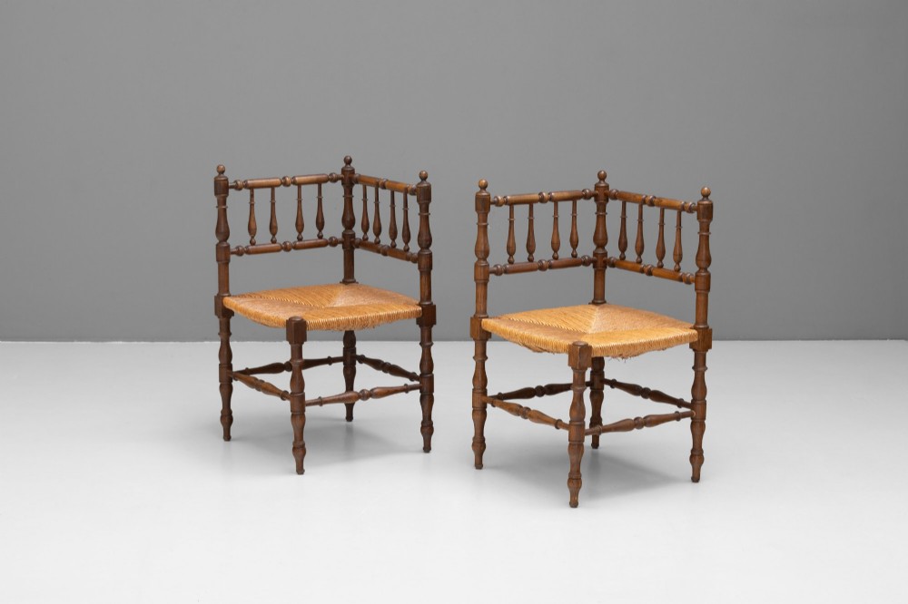 A pair of matching wooden corner chairs featuring turned bobbin spindles, raised armrests, turned leg stretchers, and square hand-woven rush seats.