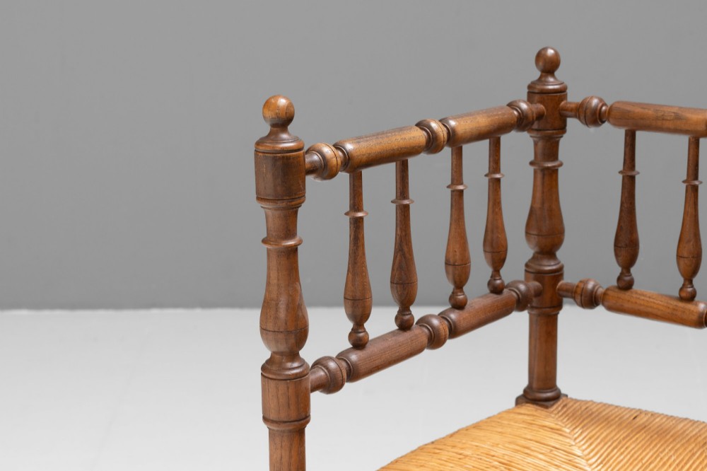 A pair of matching wooden corner chairs featuring turned bobbin spindles, raised armrests, turned leg stretchers, and square hand-woven rush seats. View V