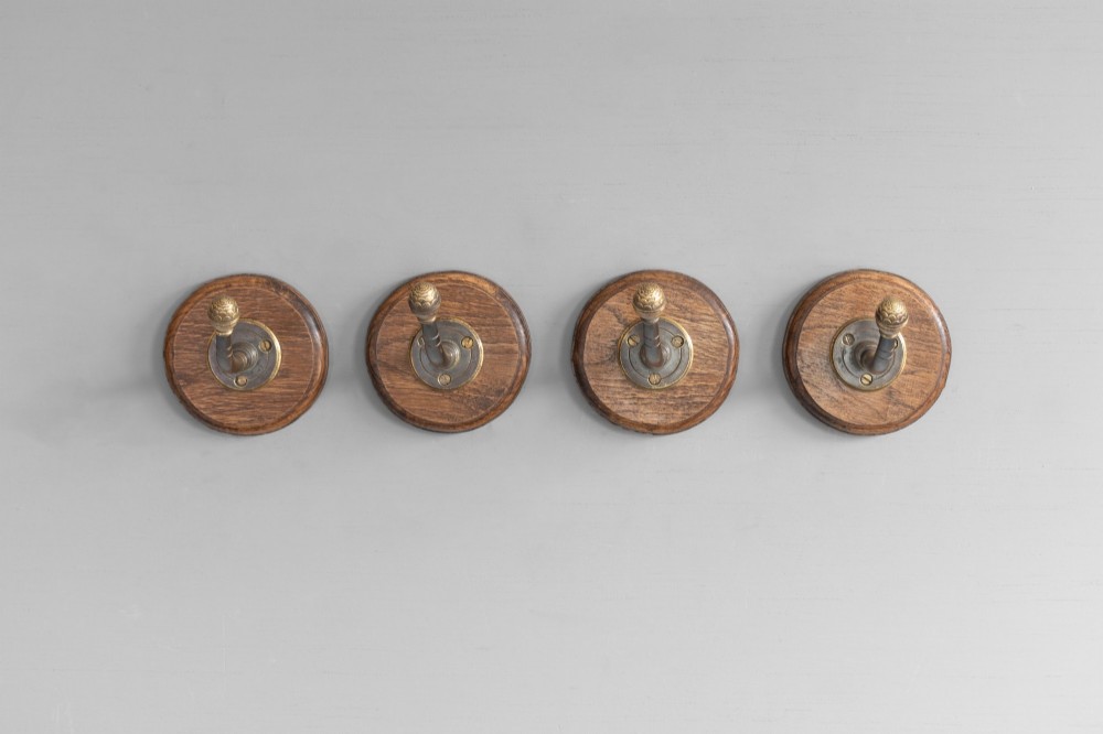 A set of four circular turned oak backplates each mounted with a central cast brass coat hook.