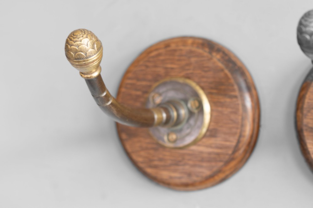 A set of four circular turned oak backplates each mounted with a central cast brass coat hook. View II