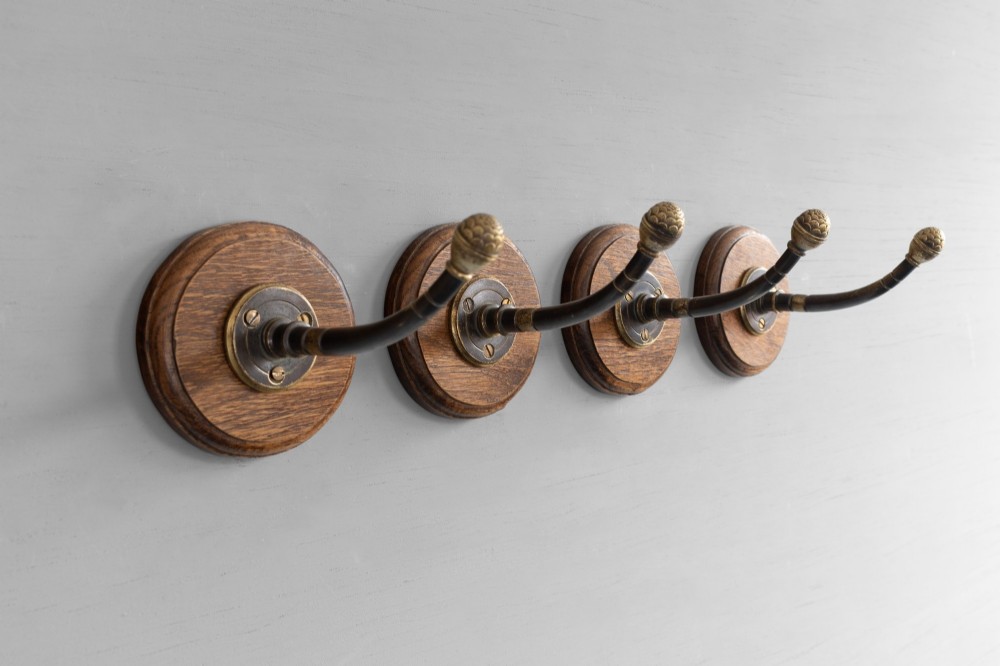 A set of four circular turned oak backplates each mounted with a central cast brass coat hook. View IV
