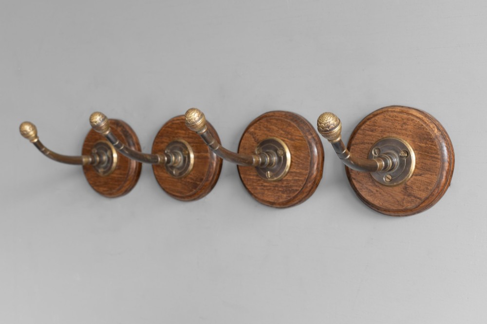 A set of four circular turned oak backplates each mounted with a central cast brass coat hook. View V