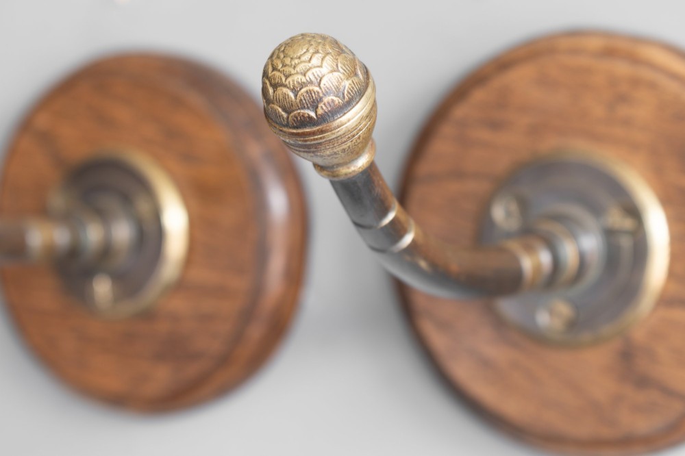 A set of four circular turned oak backplates each mounted with a central cast brass coat hook. View VI