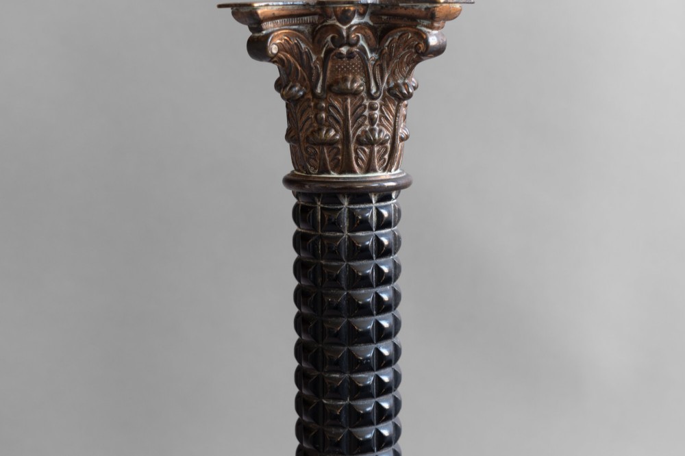 A Neoclassical style table lamp with a dark textured column shaft, an ornate brass Corinthian capital, a stepped brass base, and a grey cylindrical drum shade. View V