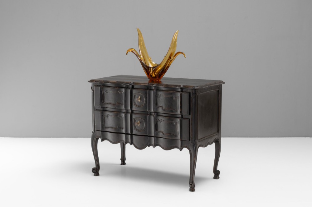 An antique dark brown painted French Rococo style commode featuring serpentine drawer fronts, cabriole legs, moulded panel details, and central brass key escutcheons.