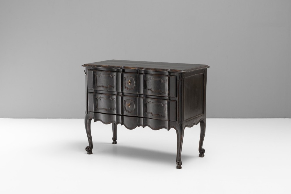 An antique dark brown painted French Rococo style commode featuring serpentine drawer fronts, cabriole legs, moulded panel details, and central brass key escutcheons. View III