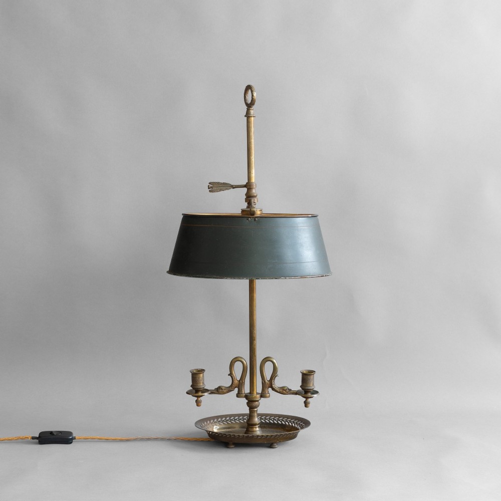 An antique French bouillotte lamp featuring a dark green metal tole shade, twin brass candle sconces, a central adjustment rod with a ring top, and a pierced dish base.