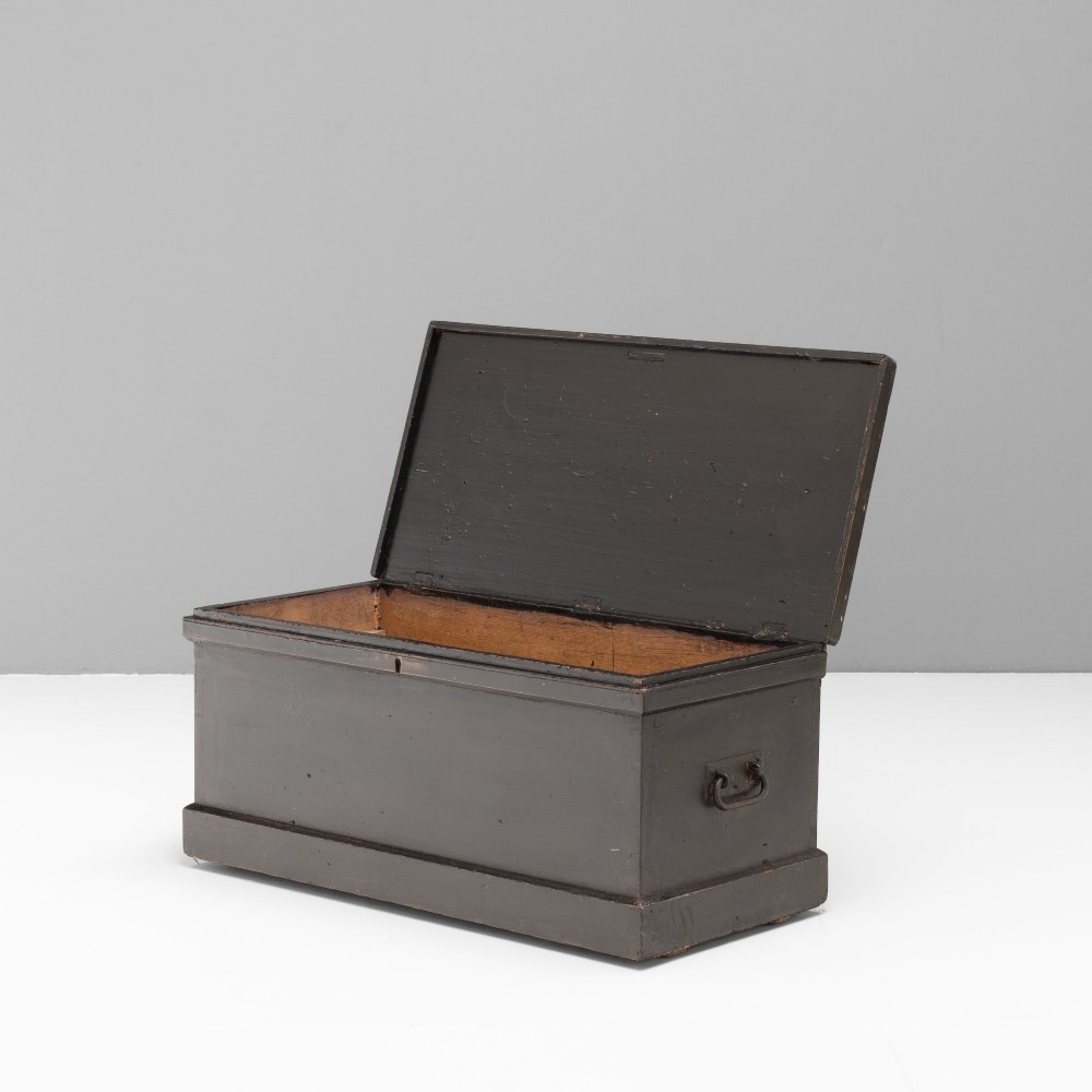 A dark painted rectangular pine storage trunk featuring an open hinged lid, natural pine interior, and iron side handles.