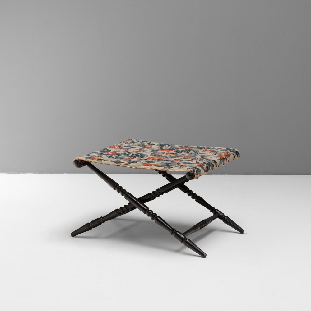 A folding dark wood luggage stand featuring an X-frame with turned legs and a floral tapestry top.