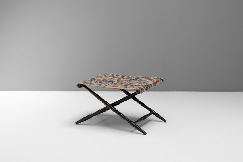 A folding dark wood luggage stand featuring an X-frame with turned legs and a floral tapestry top. View II
