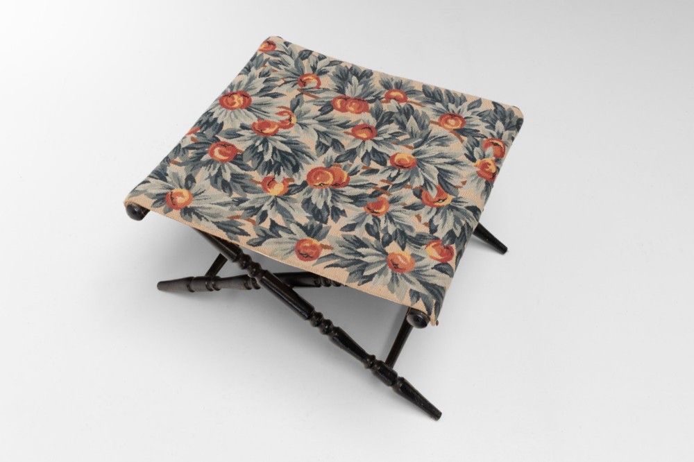 A folding dark wood luggage stand featuring an X-frame with turned legs and a floral tapestry top. View III