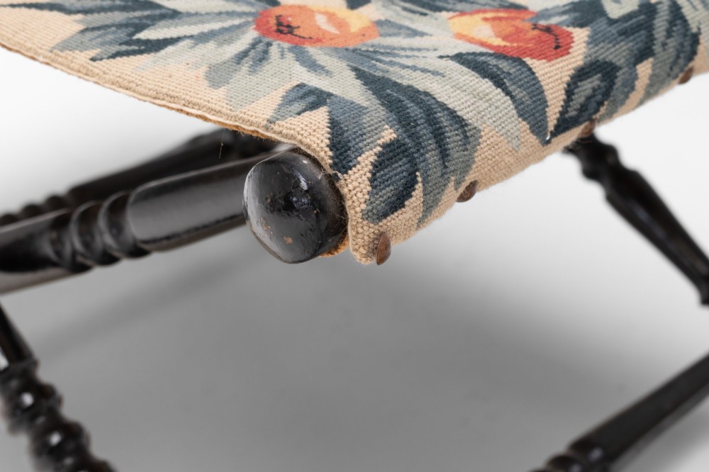 A folding dark wood luggage stand featuring an X-frame with turned legs and a floral tapestry top. View V
