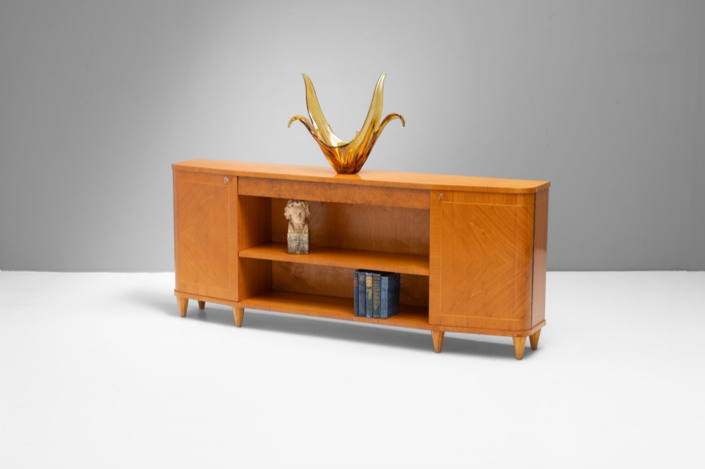 A Swedish Grace birch sideboard featuring chevron parquetry veneer doors, open central shelving, and tapered fluted feet.
