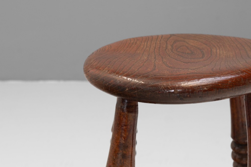 A dark brown wooden stool featuring a round seat, four lathe-turned legs, and lower connecting stretchers. View IV