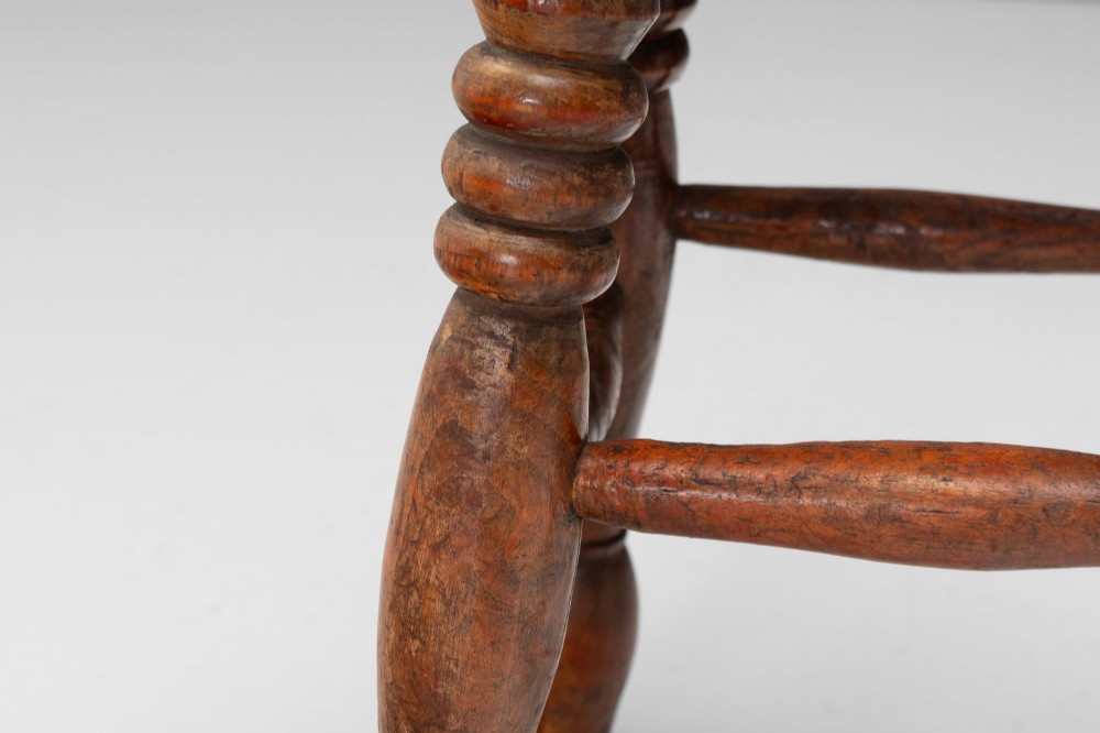 A dark brown wooden stool featuring a round seat, four lathe-turned legs, and lower connecting stretchers. View VI