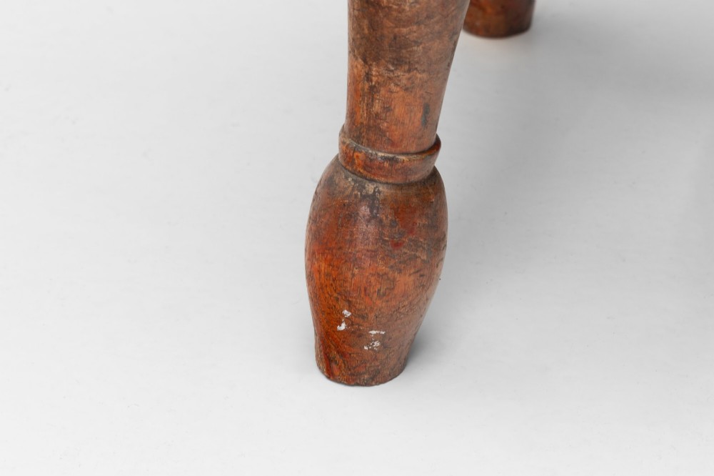 A dark brown wooden stool featuring a round seat, four lathe-turned legs, and lower connecting stretchers. View VII