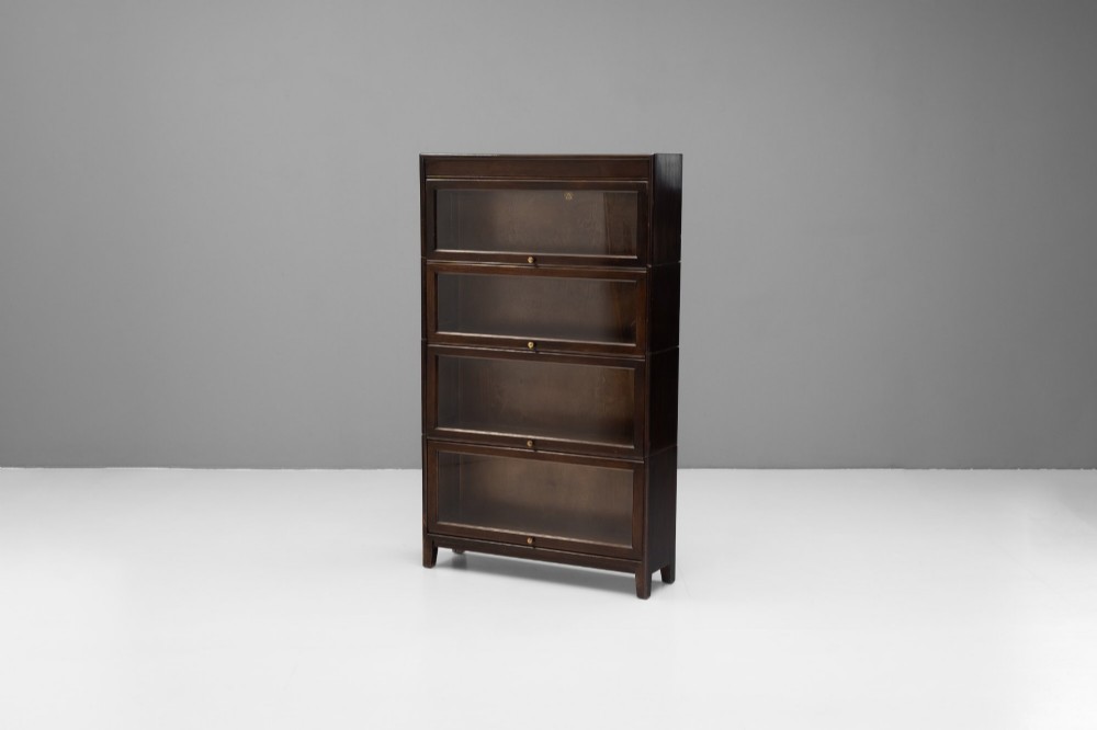 A four-tier dark wood sectional bookcase featuring glazed lift-and-slide doors with central brass knobs.