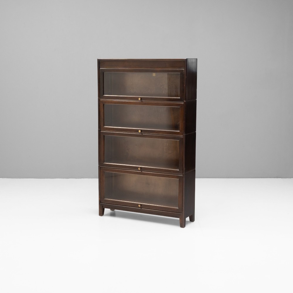 A four-tier dark wood sectional bookcase featuring glazed lift-and-slide doors with central brass knobs. View II