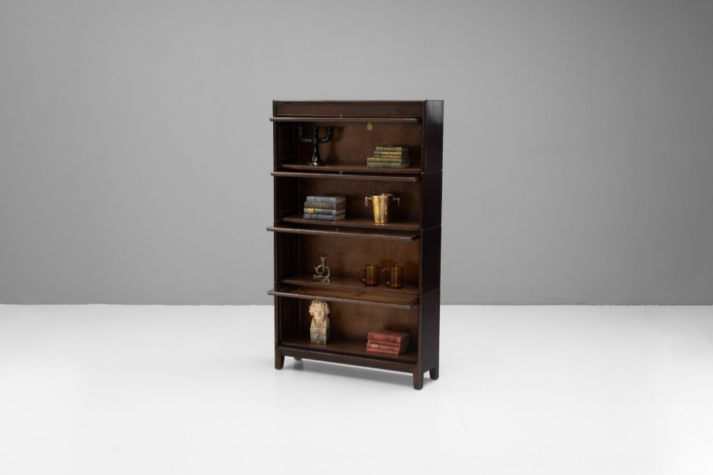 A four-tier dark wood sectional bookcase featuring glazed lift-and-slide doors with central brass knobs. View IV