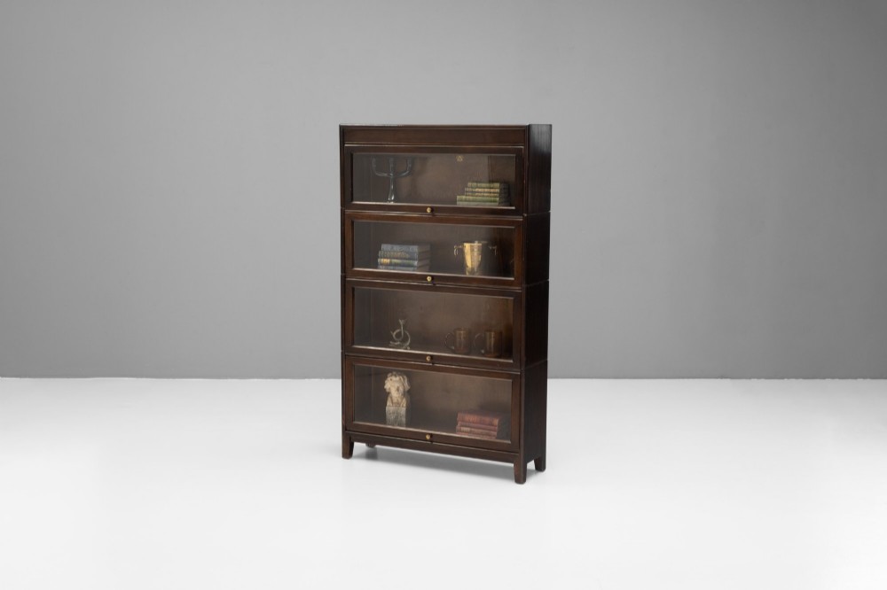 A four-tier dark wood sectional bookcase featuring glazed lift-and-slide doors with central brass knobs. View V